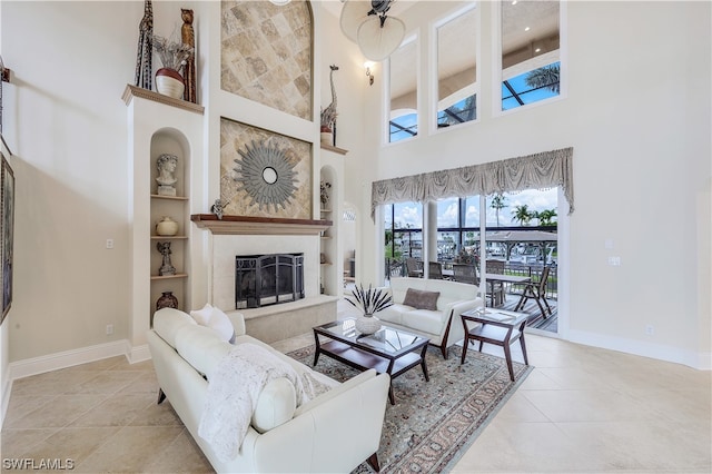 living room with light tile floors, built in shelves, a tile fireplace, and a high ceiling