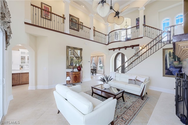 tiled living room with decorative columns, ceiling fan, and a towering ceiling