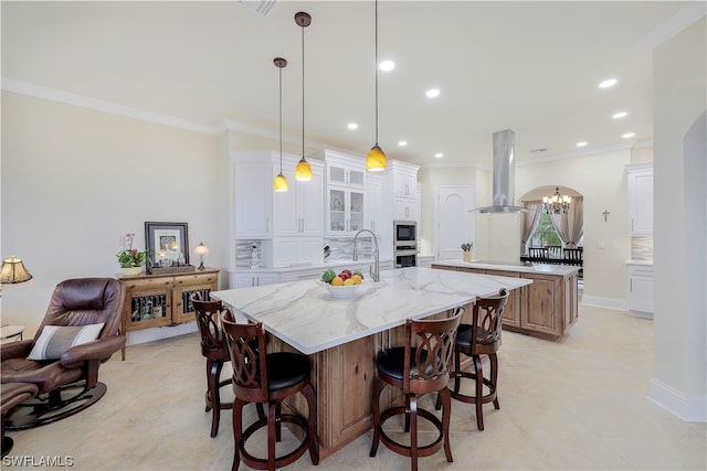 kitchen with a kitchen island with sink, light stone countertops, wall chimney exhaust hood, an inviting chandelier, and white cabinetry