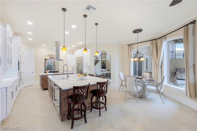 kitchen with island range hood, a chandelier, a center island with sink, white cabinetry, and hanging light fixtures