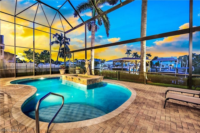 pool at dusk featuring an in ground hot tub, glass enclosure, and a patio area