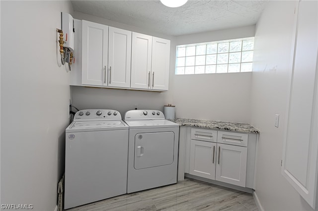 laundry area featuring light wood-type flooring, a textured ceiling, cabinets, and washer and clothes dryer