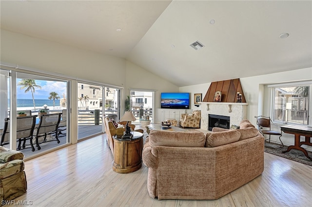 living room with a premium fireplace, a water view, vaulted ceiling, and light hardwood / wood-style flooring