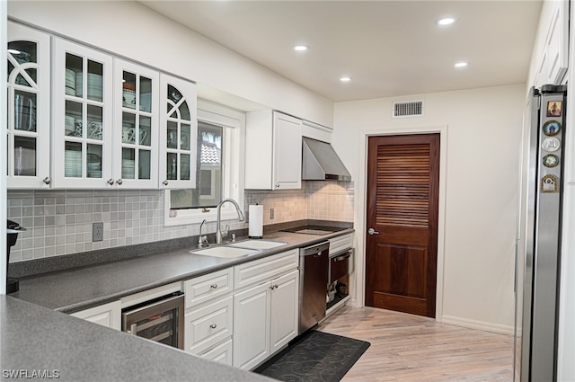 kitchen featuring wall chimney range hood, white cabinetry, light hardwood / wood-style floors, and sink