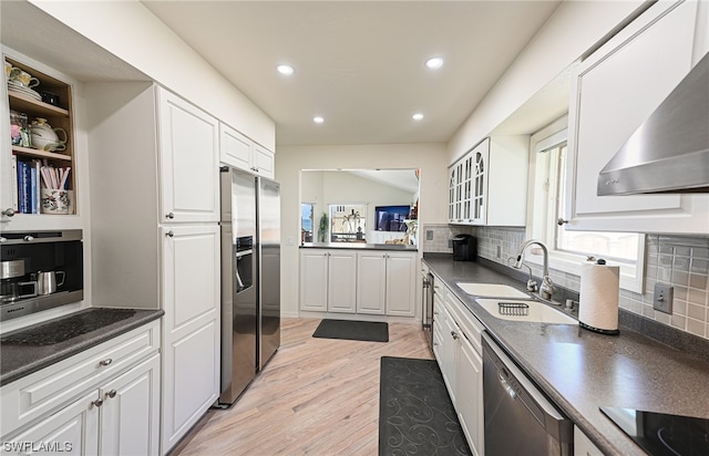 kitchen with backsplash, appliances with stainless steel finishes, light wood-type flooring, white cabinets, and wall chimney range hood