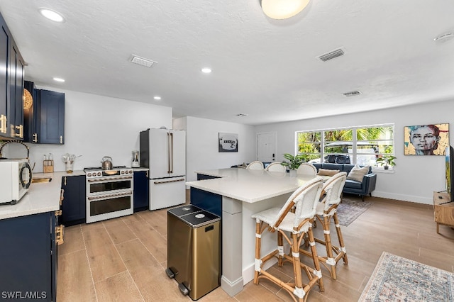 kitchen with blue cabinets, a breakfast bar, white appliances, and light wood-type flooring