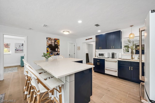 kitchen with white appliances, a kitchen breakfast bar, light hardwood / wood-style flooring, decorative light fixtures, and a center island