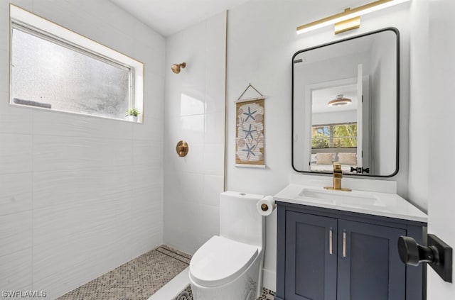 bathroom with toilet, a tile shower, and vanity