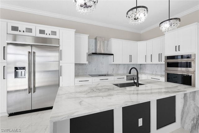 kitchen with appliances with stainless steel finishes, wall chimney exhaust hood, sink, decorative light fixtures, and white cabinetry