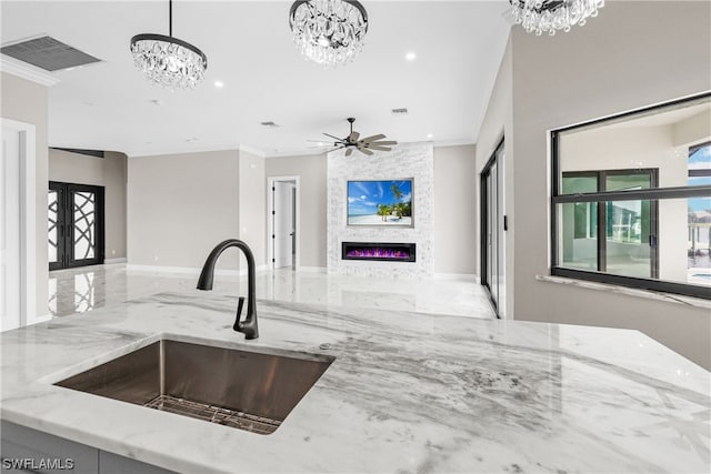 kitchen with sink, a stone fireplace, light stone counters, decorative light fixtures, and ornamental molding