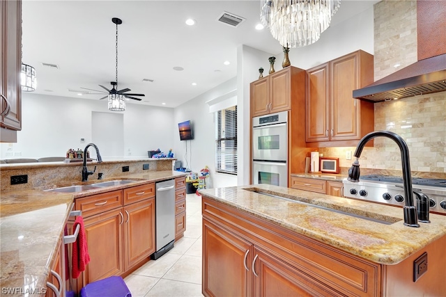 kitchen with stainless steel appliances, light stone countertops, ceiling fan with notable chandelier, wall chimney exhaust hood, and backsplash