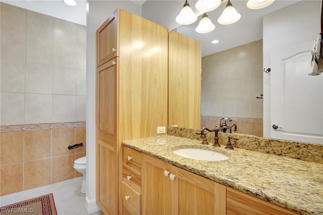 bathroom with tile walls, toilet, large vanity, and tile flooring