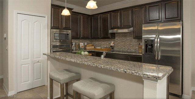 kitchen featuring light stone counters, stainless steel appliances, decorative light fixtures, and dark brown cabinets