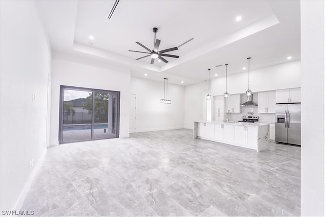 unfurnished living room featuring light tile floors, a tray ceiling, ceiling fan, and sink