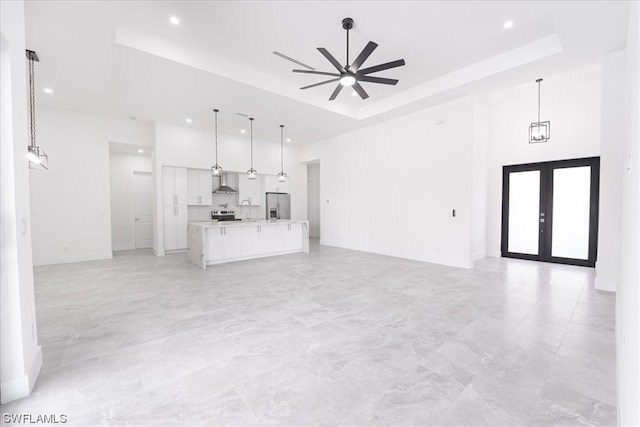 unfurnished living room featuring french doors, ceiling fan, a raised ceiling, light tile flooring, and a high ceiling