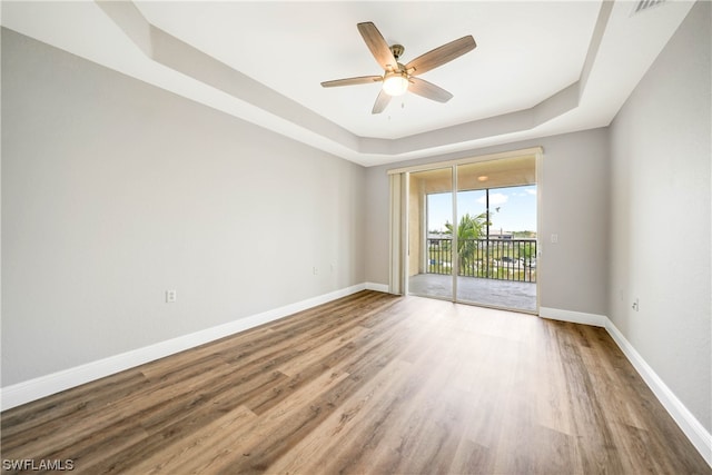 unfurnished room with a raised ceiling, wood-type flooring, and ceiling fan