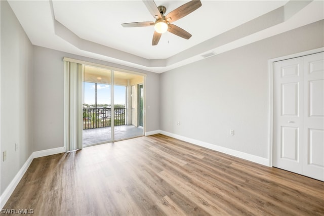 empty room with a tray ceiling, ceiling fan, and wood-type flooring