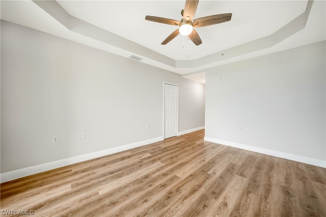 empty room featuring a raised ceiling, ceiling fan, and light wood-type flooring