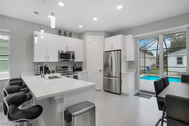 kitchen with a breakfast bar, hanging light fixtures, white cabinetry, and stainless steel appliances