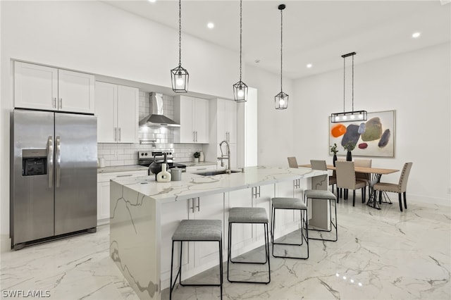 kitchen with decorative light fixtures, appliances with stainless steel finishes, backsplash, an island with sink, and wall chimney exhaust hood