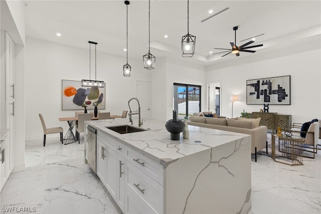 kitchen with hanging light fixtures, a tray ceiling, a kitchen island with sink, white cabinets, and sink