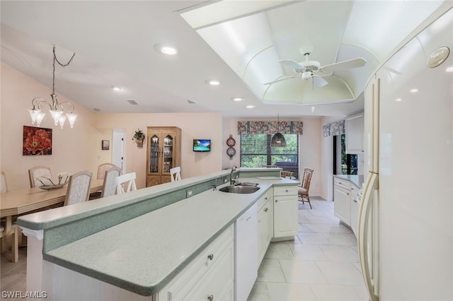 kitchen with sink, a large island with sink, white appliances, white cabinets, and ceiling fan with notable chandelier