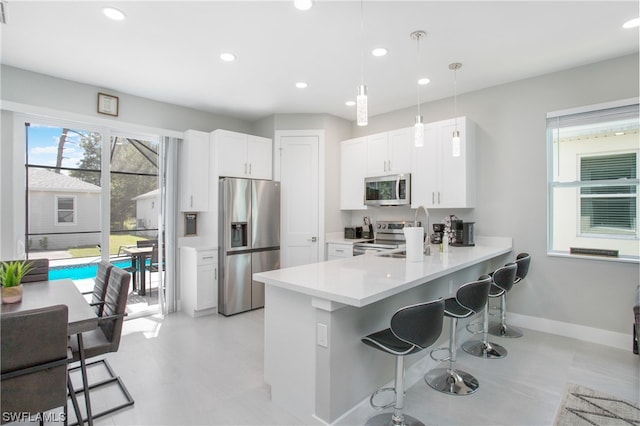 kitchen with a kitchen breakfast bar, hanging light fixtures, white cabinets, and appliances with stainless steel finishes