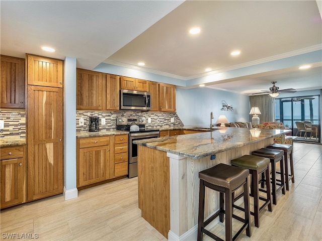 kitchen with tasteful backsplash, stainless steel appliances, ceiling fan, and a kitchen breakfast bar