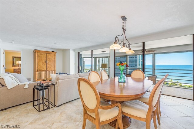 dining space featuring light tile floors, a water view, ornamental molding, and a chandelier