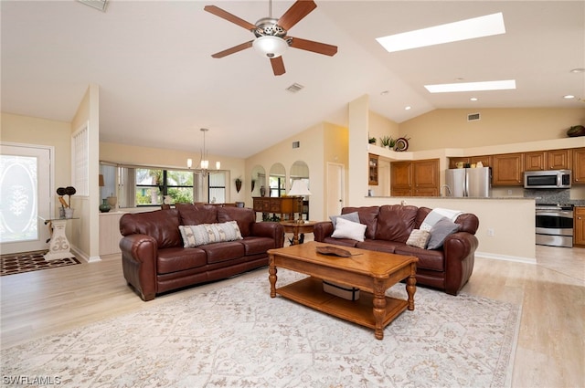 living room featuring ceiling fan with notable chandelier, light wood-type flooring, a skylight, and high vaulted ceiling