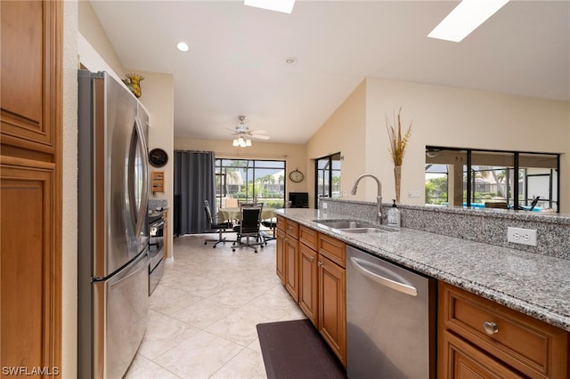 kitchen with ceiling fan, sink, light stone countertops, vaulted ceiling with skylight, and appliances with stainless steel finishes