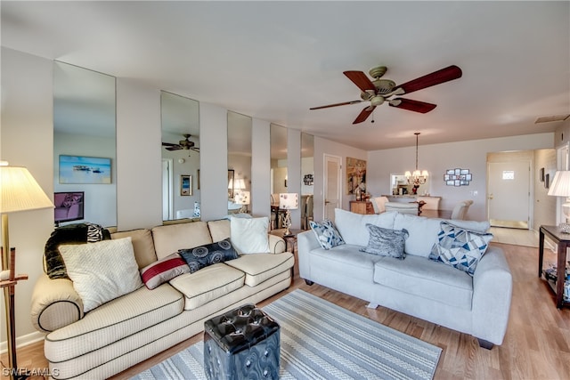 living room featuring ceiling fan with notable chandelier and light wood-type flooring