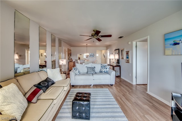 living room featuring ceiling fan with notable chandelier and light hardwood / wood-style flooring