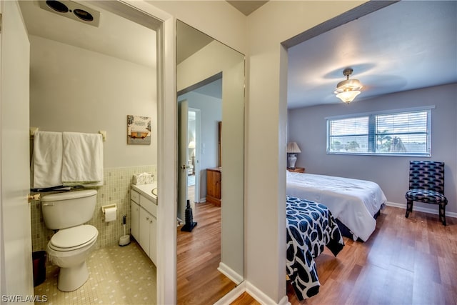 bedroom with ceiling fan, light wood-type flooring, and tile walls