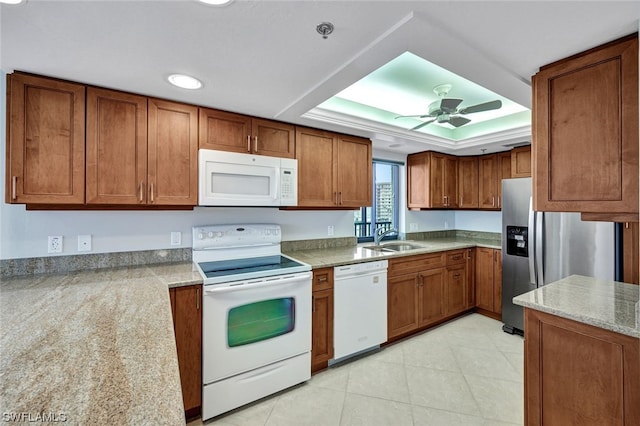 kitchen featuring white appliances, a raised ceiling, sink, ceiling fan, and light stone counters