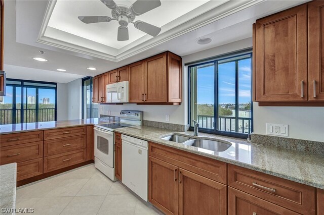 kitchen featuring light stone counters, white appliances, a tray ceiling, ceiling fan, and sink