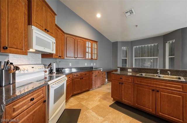 kitchen featuring white appliances, sink, light tile floors, dark stone countertops, and vaulted ceiling