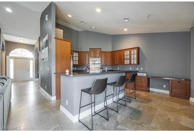 kitchen featuring high vaulted ceiling, light tile floors, a center island with sink, a breakfast bar area, and dark stone countertops