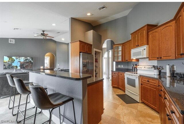 kitchen with a breakfast bar area, ceiling fan, white appliances, and high vaulted ceiling