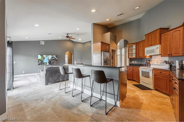 kitchen featuring white appliances, ceiling fan, a kitchen breakfast bar, light tile flooring, and high vaulted ceiling