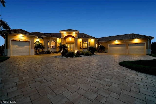 mediterranean / spanish-style home with an attached garage, a tile roof, decorative driveway, and stucco siding