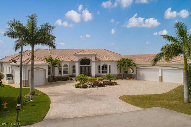 mediterranean / spanish home featuring an attached garage, a tile roof, decorative driveway, and stucco siding