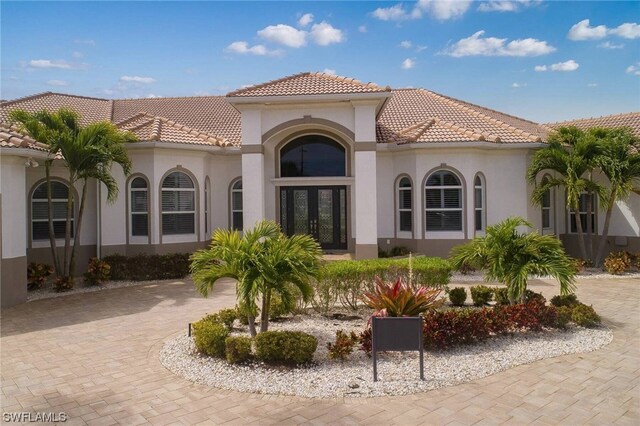 back of house with a tile roof, french doors, decorative driveway, and stucco siding