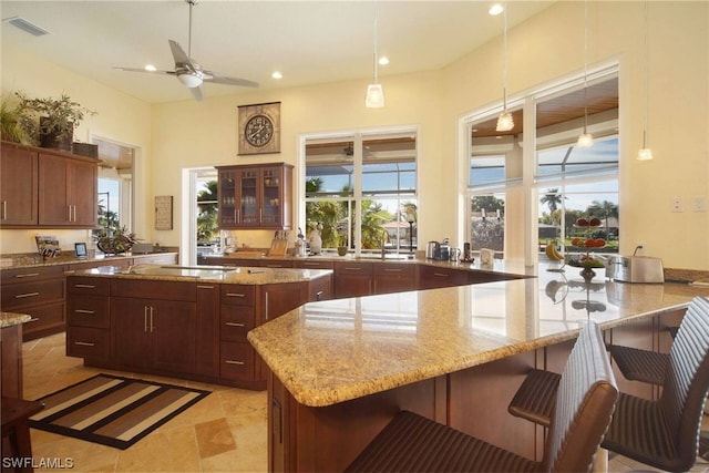 kitchen featuring glass insert cabinets, visible vents, a breakfast bar, and light stone counters