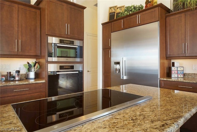 kitchen with built in fridge, light stone counters, and black electric stovetop