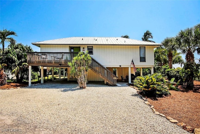 back of house with metal roof, a carport, gravel driveway, and stairway