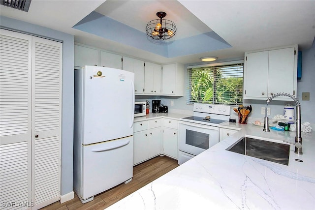 kitchen with a tray ceiling, white appliances, hardwood / wood-style floors, and light stone countertops