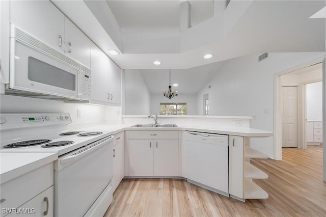 kitchen featuring a peninsula, white appliances, light countertops, and a sink