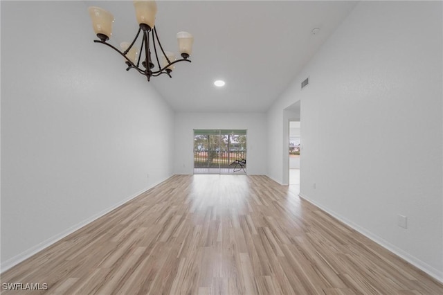 unfurnished living room featuring light wood finished floors, baseboards, visible vents, an inviting chandelier, and high vaulted ceiling