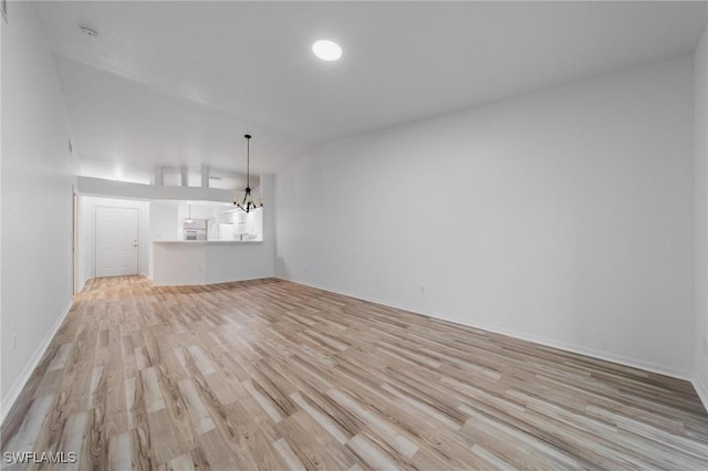 unfurnished living room featuring vaulted ceiling, light wood-type flooring, baseboards, and a notable chandelier